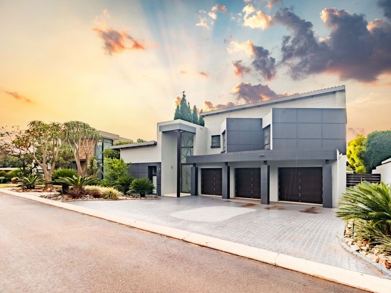 Modern architectural home featuring a triple garage, paved driveway, and well-maintained landscaped garden, presented with a striking sunset backdrop.