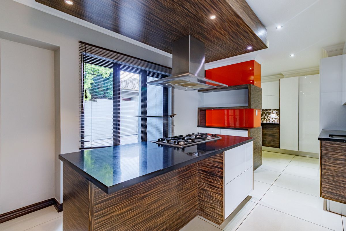 Modern kitchen featuring a central island with a gas cooktop, stainless steel extractor fan, high-gloss cabinetry, and sleek stone countertops.