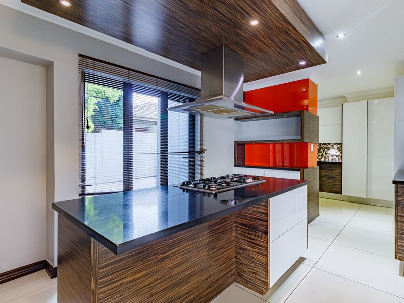 Modern kitchen featuring a central island with a gas cooktop, stainless steel extractor fan, high-gloss cabinetry, and sleek stone countertops.