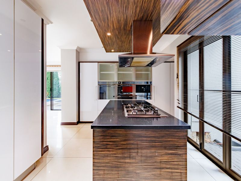 Modern kitchen featuring a central island with gas hob, integrated extractor fan, built-in ovens, and sleek cabinetry with stone countertops.