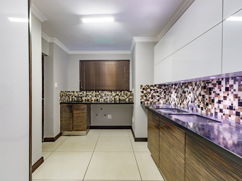 Modern kitchen featuring high-gloss white upper cabinets, wood-grain lower cabinetry, mosaic tile backsplash, stone countertops, and a double basin sink.