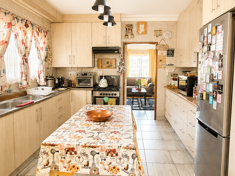 A functional kitchen featuring light wood-finish cabinetry, a gas stove with extractor fan, double sink, and tiled flooring, offering ample storage and workspace.