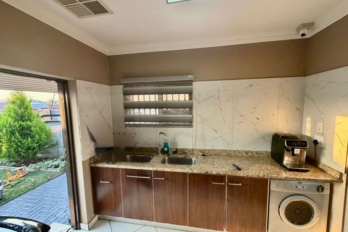 Kitchen area featuring granite countertops, double stainless steel sink, and marble-look splashback with direct access to the outdoor patio area.