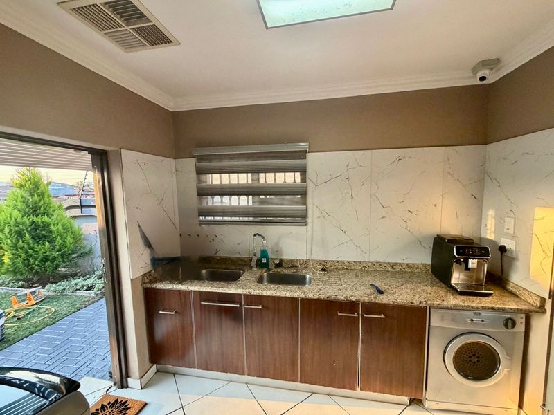 Kitchen area featuring granite countertops, double stainless steel sink, and marble-look splashback with direct access to the outdoor patio area.