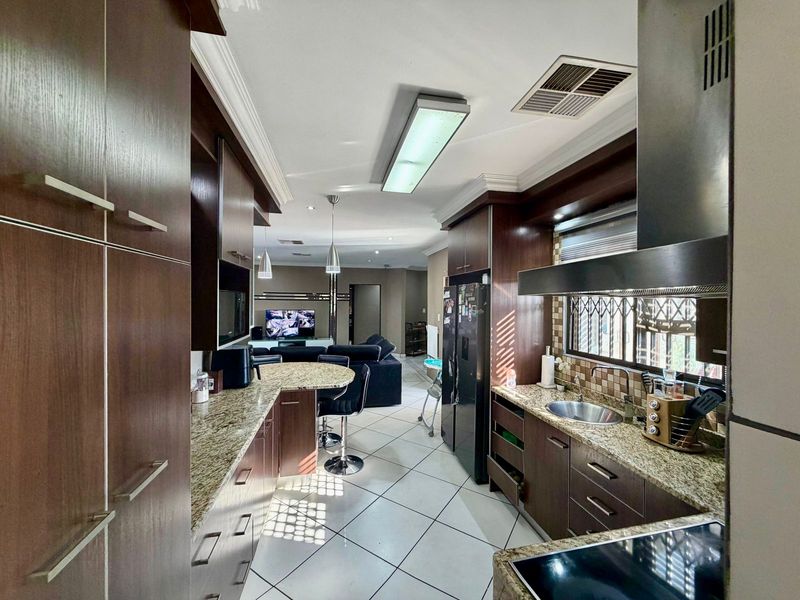 Open-plan kitchen and living area featuring dark wood cabinetry, granite countertops, tiled flooring, and integrated kitchen fixtures.