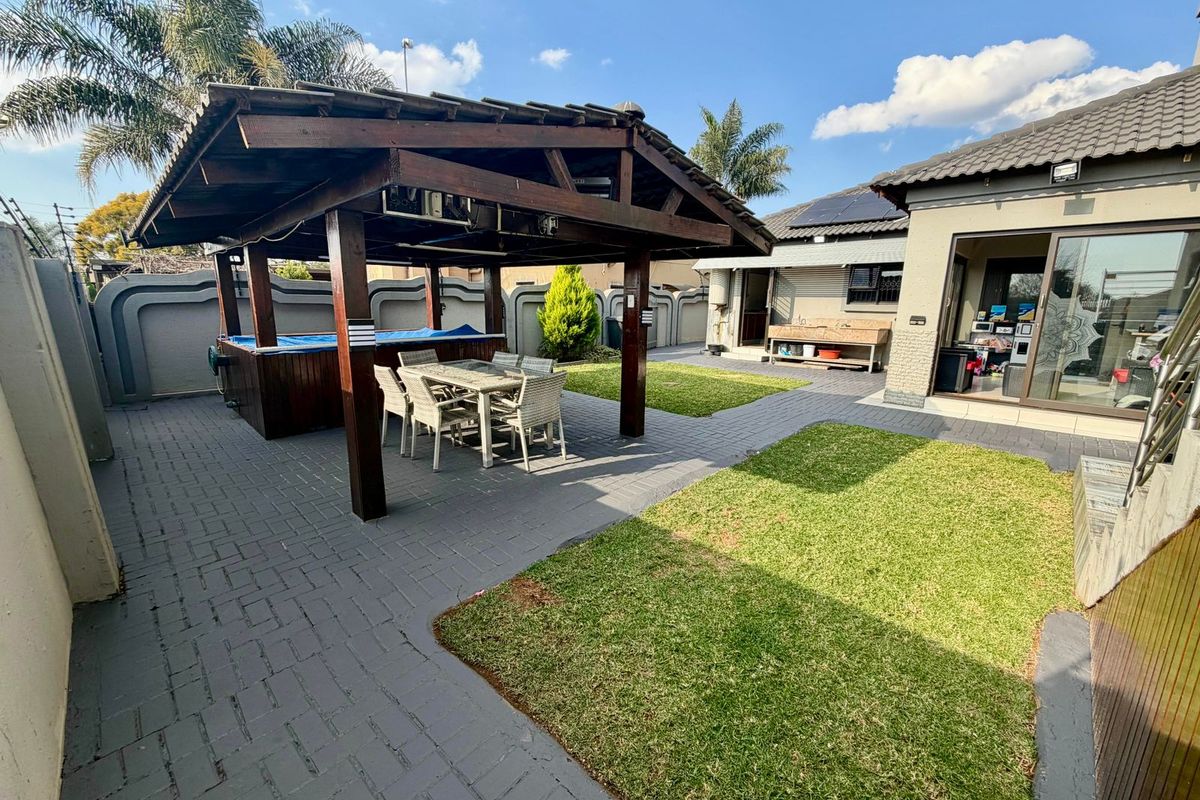 A well-maintained rear garden featuring a timber gazebo with a built-in jacuzzi, paved patio area, and manicured lawn.