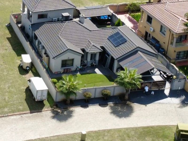 Aerial view of a residential property featuring a tiled roof, solar panels, a paved driveway, and a private garden with a covered patio area.