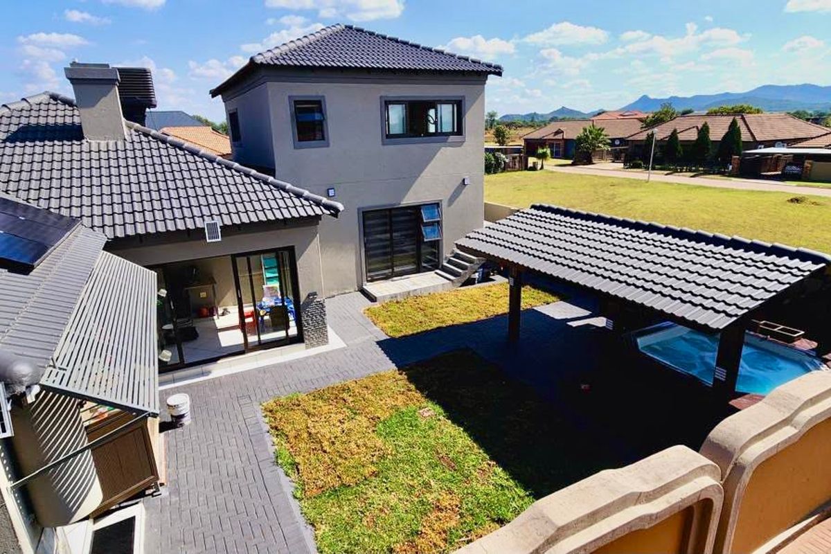 Aerial view of a modern residential property featuring a tiled roof with solar panels, a paved courtyard, and a covered patio with a swimming pool.