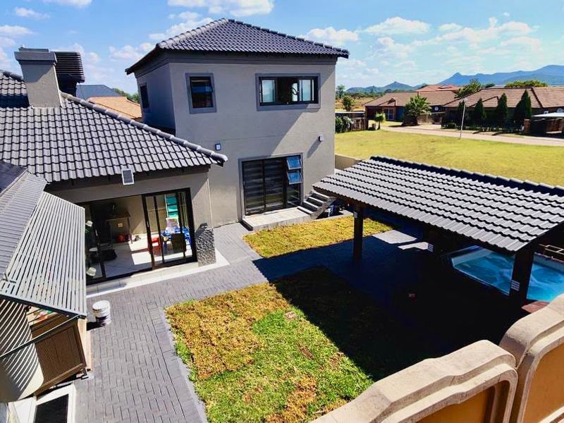 Aerial view of a modern residential property featuring a tiled roof with solar panels, a paved courtyard, and a covered patio with a swimming pool.