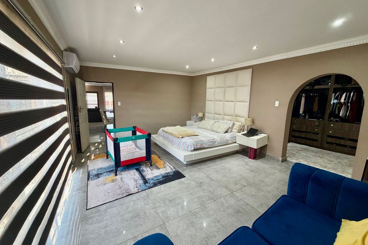 Spacious bedroom featuring tiled flooring, recessed downlighting, an air conditioning unit, and a dedicated walk-in closet area accessed through an elegant archway.