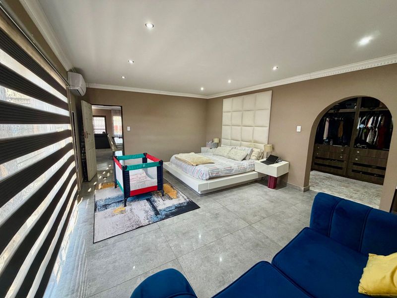 Spacious bedroom featuring tiled flooring, recessed downlighting, an air conditioning unit, and a dedicated walk-in closet area accessed through an elegant archway.