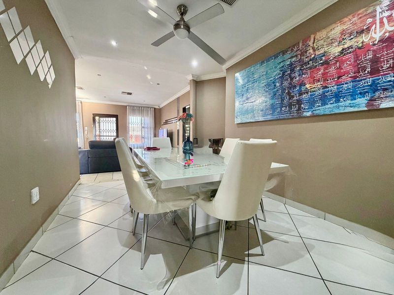 A well-lit dining area featuring tiled flooring, coved cornicing, and a ceiling fan, flowing into an adjacent living space.