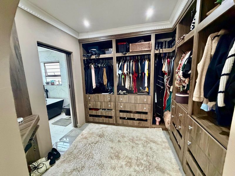 A well-appointed walk-in closet featuring extensive built-in wooden cabinetry with integrated shelving and hanging space, leading directly into a modern bathroom.
