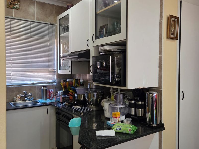 A compact kitchen featuring granite countertops, built-in cabinetry, a built-in oven with hob, and a tiled backsplash.