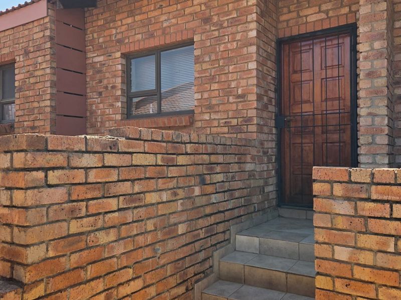 Front entrance of a townhouse featuring face brick construction, tiled steps, and a secure wooden door with a metal security gate.