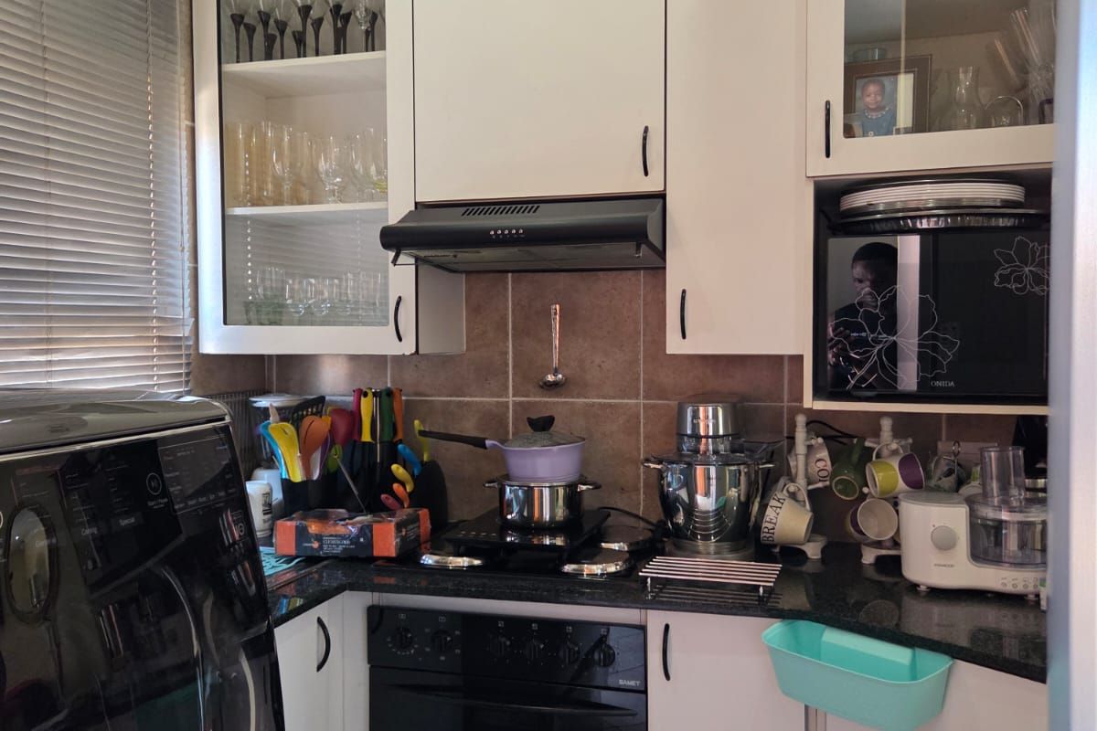 Compact kitchen featuring white cabinetry, granite countertops, tiled backsplash, and integrated appliances including an oven and extractor fan.