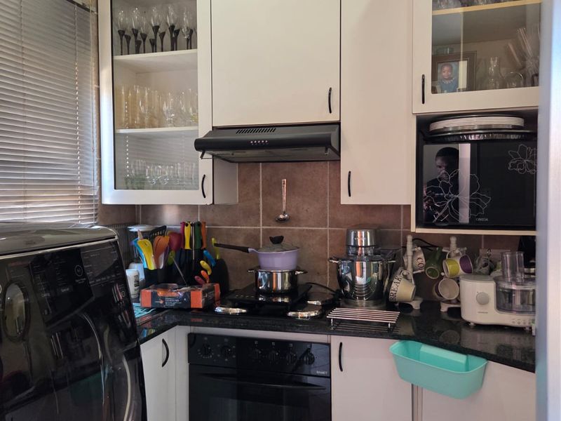 Compact kitchen featuring white cabinetry, granite countertops, tiled backsplash, and integrated appliances including an oven and extractor fan.