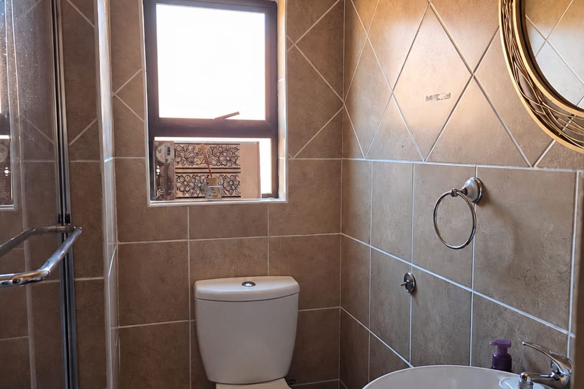 Compact bathroom featuring a shower enclosure, vessel sink vanity, and tiled finishes. The space includes a toilet with visible plumbing.