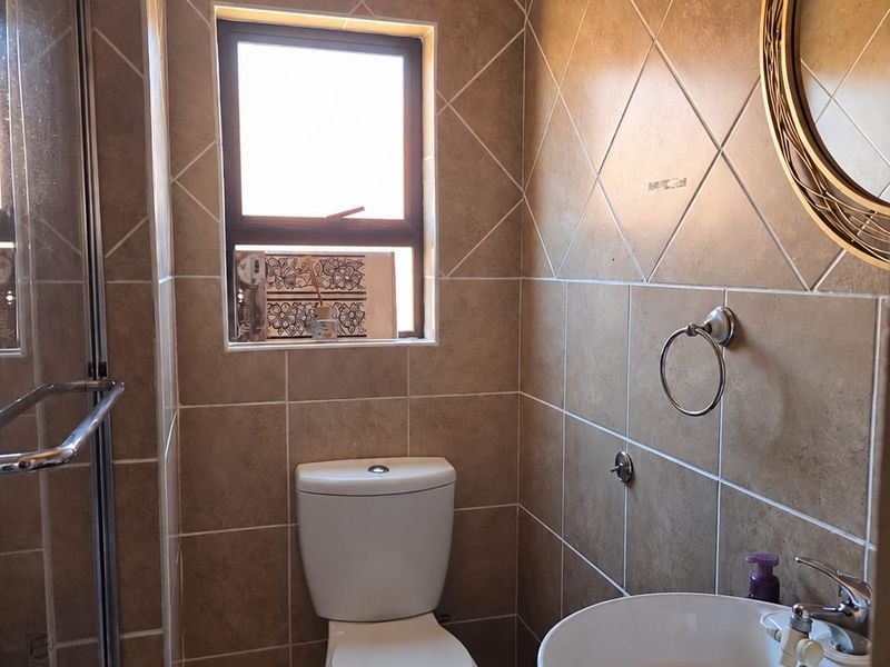 Compact bathroom featuring a shower enclosure, vessel sink vanity, and tiled finishes. The space includes a toilet with visible plumbing.