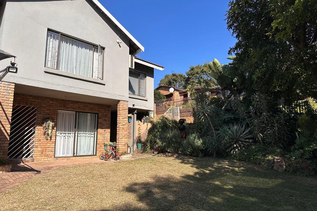 Rear view of the house featuring a brick and plaster facade, sliding glass doors leading to a paved patio, and a well-maintained garden area.