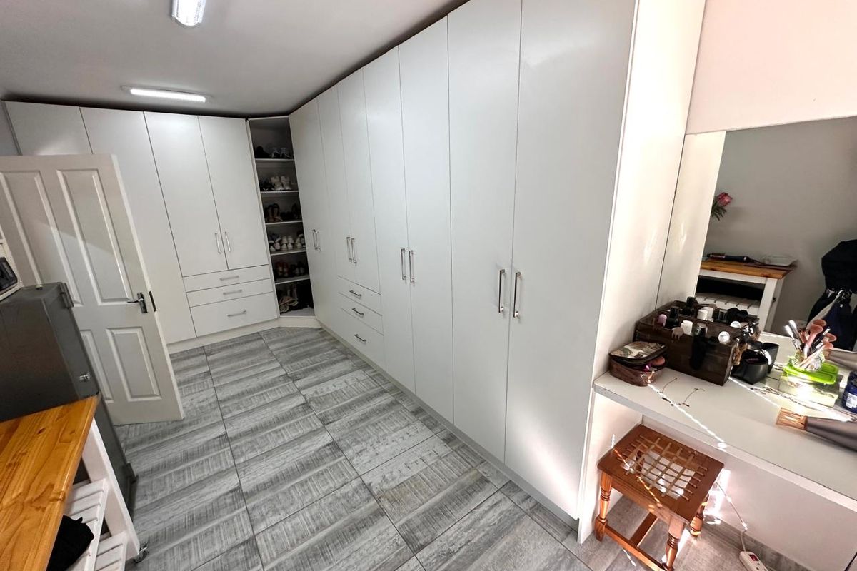 A well-organized bedroom featuring extensive floor-to-ceiling built-in wardrobes, tiled flooring, and a dedicated vanity area with integrated mirror.