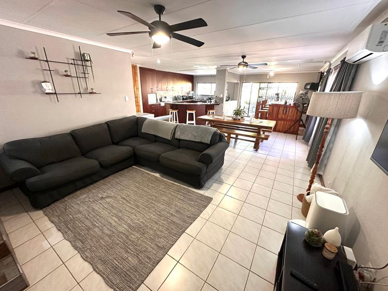 Spacious open-plan living area featuring tiled floors, ceiling fans, and a functional kitchen with a breakfast bar, flowing towards a rear sliding door.