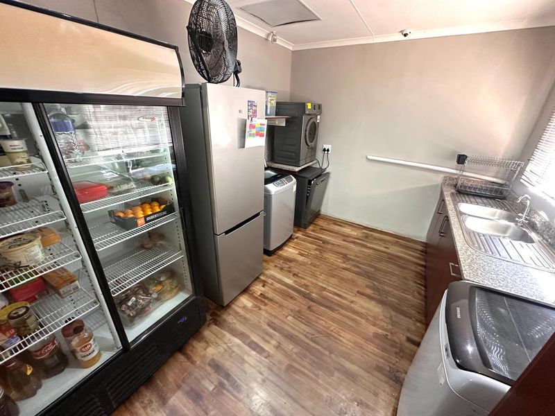 A functional scullery area featuring laminate wood flooring, granite countertops, a double bowl stainless steel sink, and ample space for laundry and refrigeration appliances.