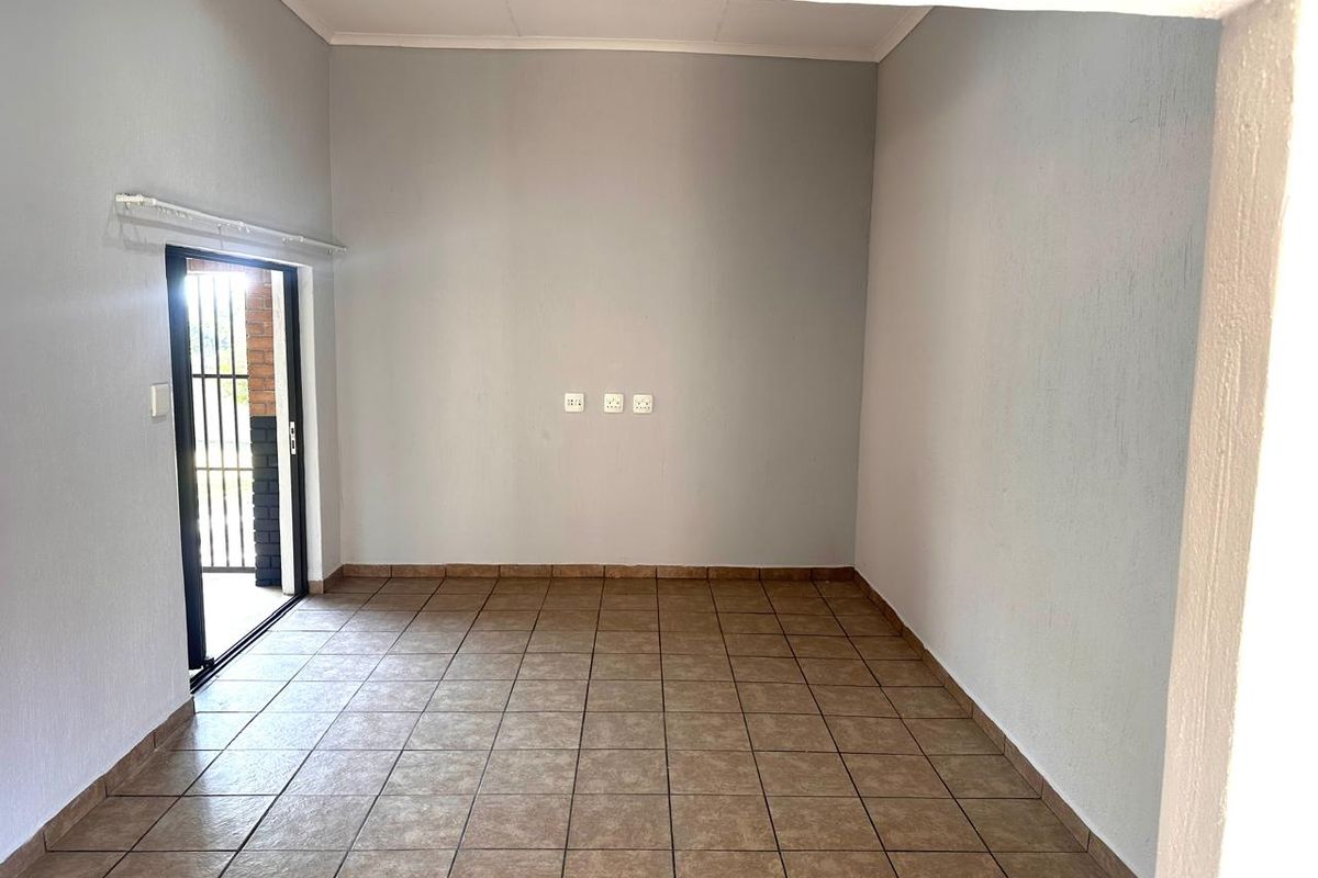 An empty, neutrally painted living area featuring tiled flooring and a sliding glass door providing access to the exterior.