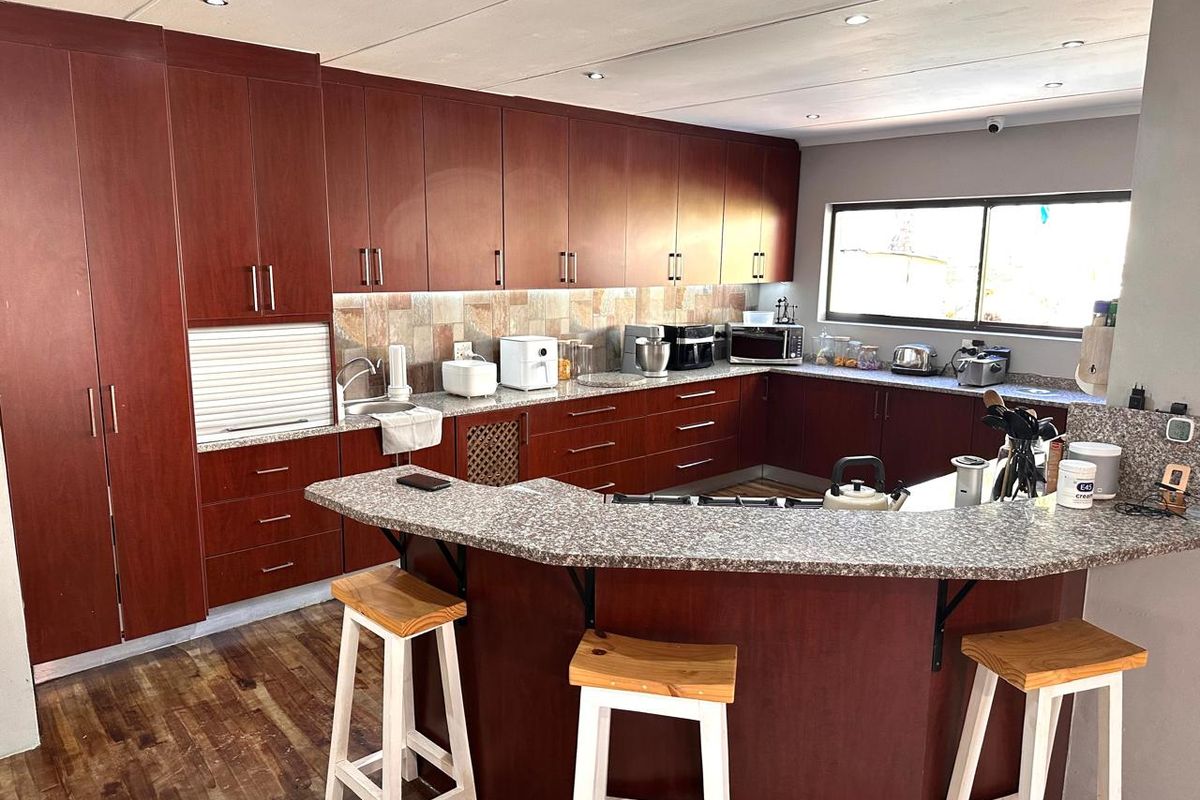 Spacious kitchen featuring extensive dark wood cabinetry, granite countertops, a breakfast bar, and stone tile backsplash with recessed lighting.