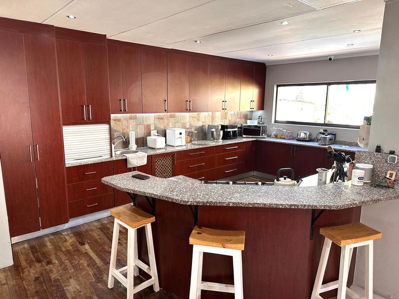 Spacious kitchen featuring extensive dark wood cabinetry, granite countertops, a breakfast bar, and stone tile backsplash with recessed lighting.