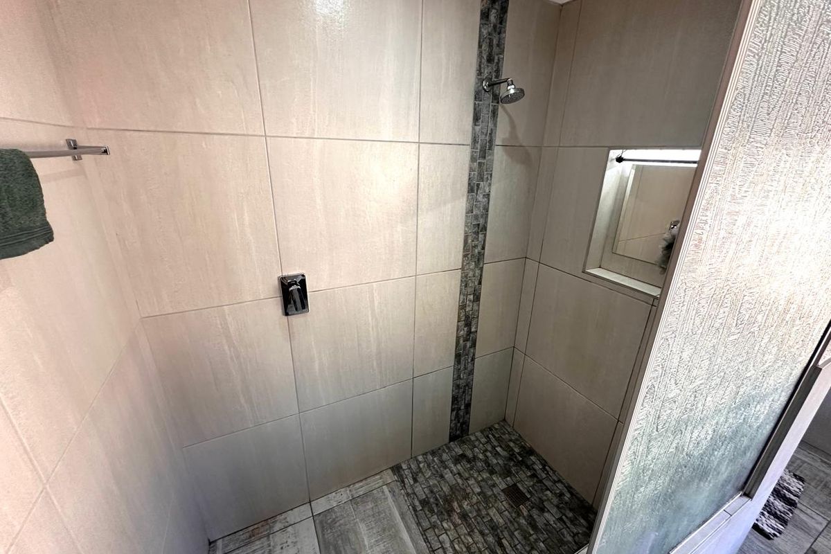 A modern walk-in shower featuring neutral wall tiles, a decorative mosaic accent strip, a built-in niche, and a stone-look tiled floor.