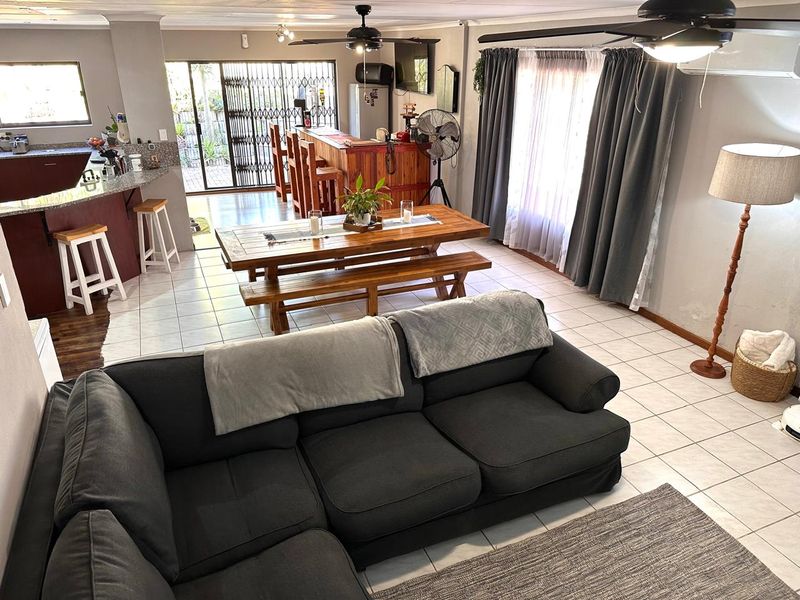 Spacious open-plan living and dining area featuring tiled floors, a breakfast bar, and direct access to the rear exterior through a security gate.