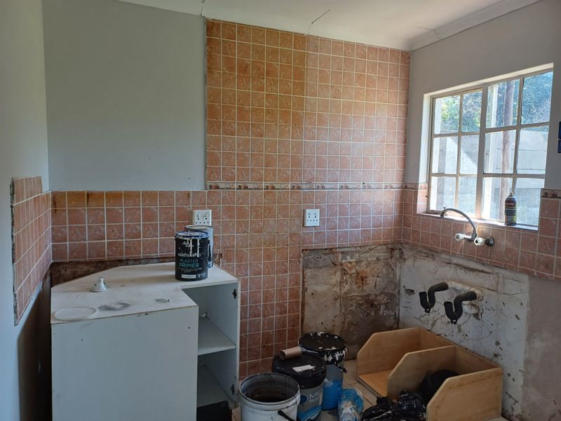 A kitchen space currently undergoing renovation, featuring tiled splashbacks, a window, and exposed plumbing connections ready for new cabinetry and fixtures.