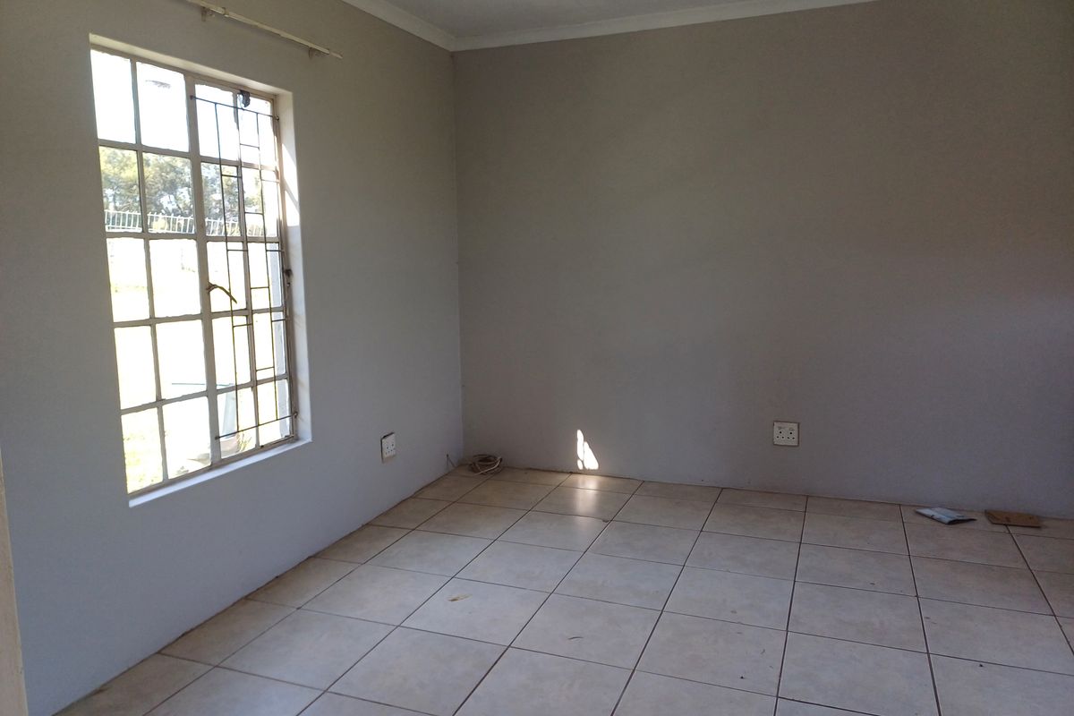 An empty bedroom featuring neutral painted walls, tiled flooring, and a window fitted with security bars.