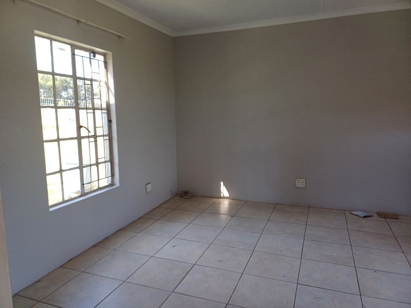 An empty bedroom featuring neutral painted walls, tiled flooring, and a window fitted with security bars.