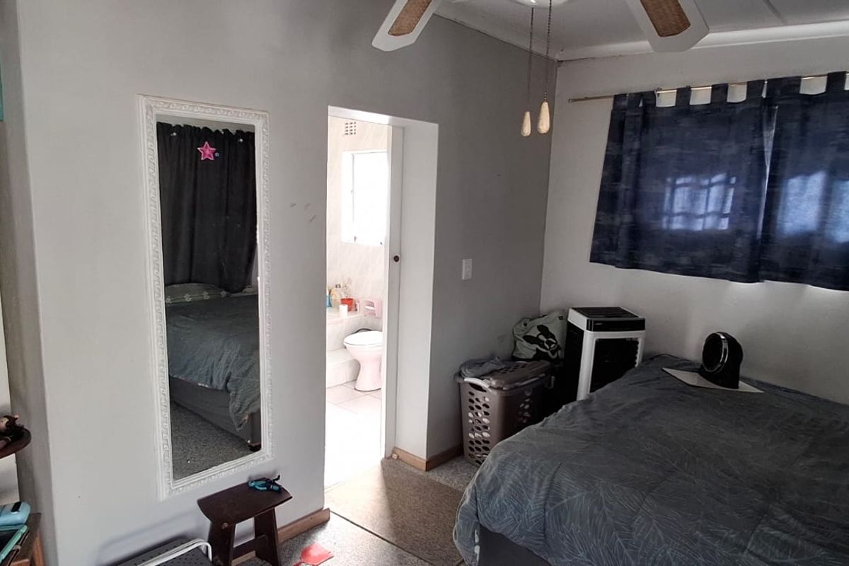 A bedroom featuring a ceiling fan and an adjoining en-suite bathroom, with neutral wall finishes and standard window treatments.