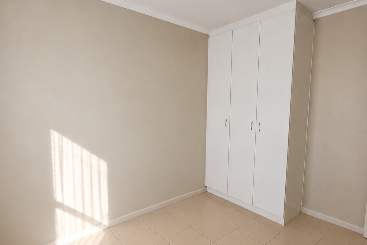 A bright, empty bedroom featuring neutral wall tones, tiled flooring, and a white built-in wardrobe.