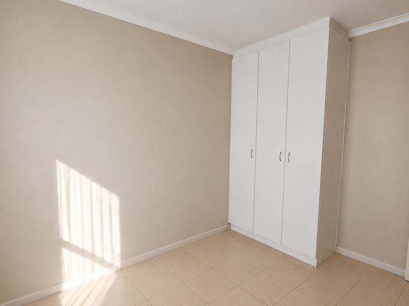 A bright, empty bedroom featuring neutral wall tones, tiled flooring, and a white built-in wardrobe.