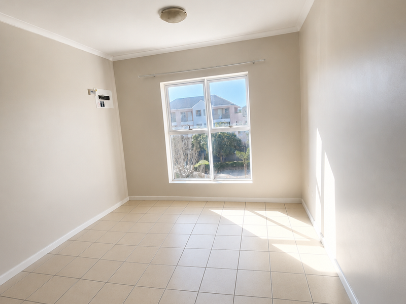 A bright, empty bedroom featuring neutral tiled flooring, a central ceiling light, and a window providing natural light and neighborhood views.