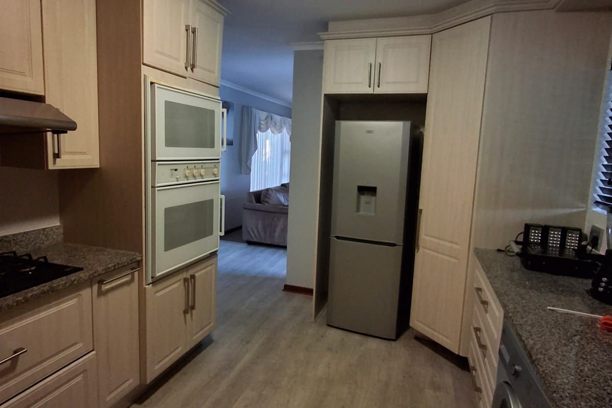 A functional kitchen featuring light-toned cabinetry, granite countertops, built-in oven and microwave, and durable laminate flooring with a view into the adjacent living area.