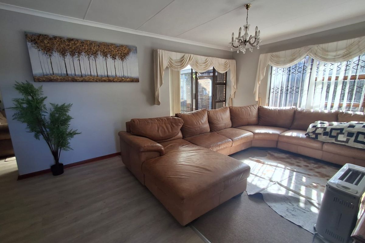 A well-maintained living room featuring laminate flooring, coved ceilings, a decorative chandelier, and sliding glass doors leading to an outdoor area.