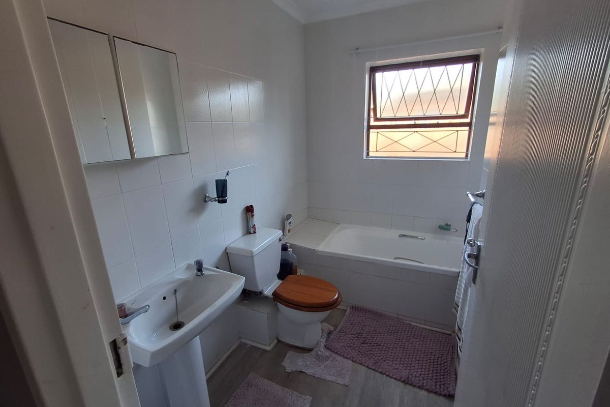 A functional bathroom featuring a pedestal sink, built-in bathtub, toilet, and tiled wall finishes with a window providing natural light.