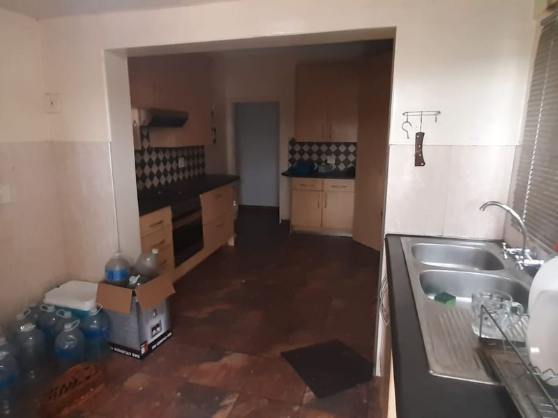 A functional kitchen featuring built-in cabinetry, a double bowl stainless steel sink, built-in oven, and extractor fan, with tiled flooring and splashbacks.