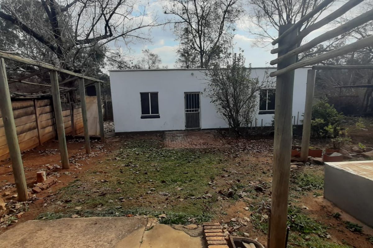 Rear exterior view of the property featuring a timber pergola structure, a small garden area, and a concrete plinth, requiring landscaping and maintenance.