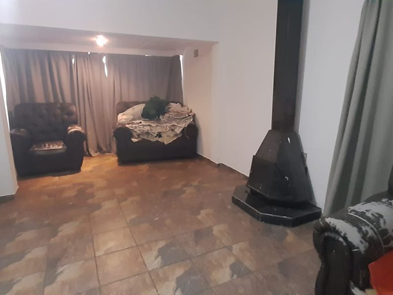 A living room area featuring tiled flooring and a black freestanding fireplace, offering a functional space with potential for modernization.