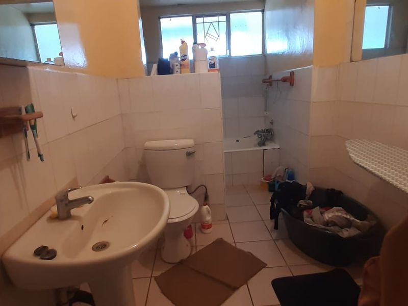 A dated bathroom featuring a pedestal basin, toilet, and bathtub with white ceramic wall and floor tiles.