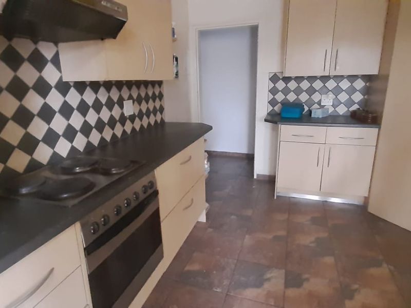 A functional kitchen featuring built-in cabinetry, a dark laminate countertop, an electric hob with an extractor fan, and tiled flooring.
