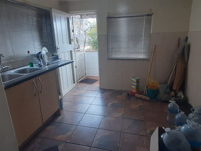 A functional scullery area featuring a double bowl sink, laminate cabinetry, and tiled flooring with direct access to an exterior space.
