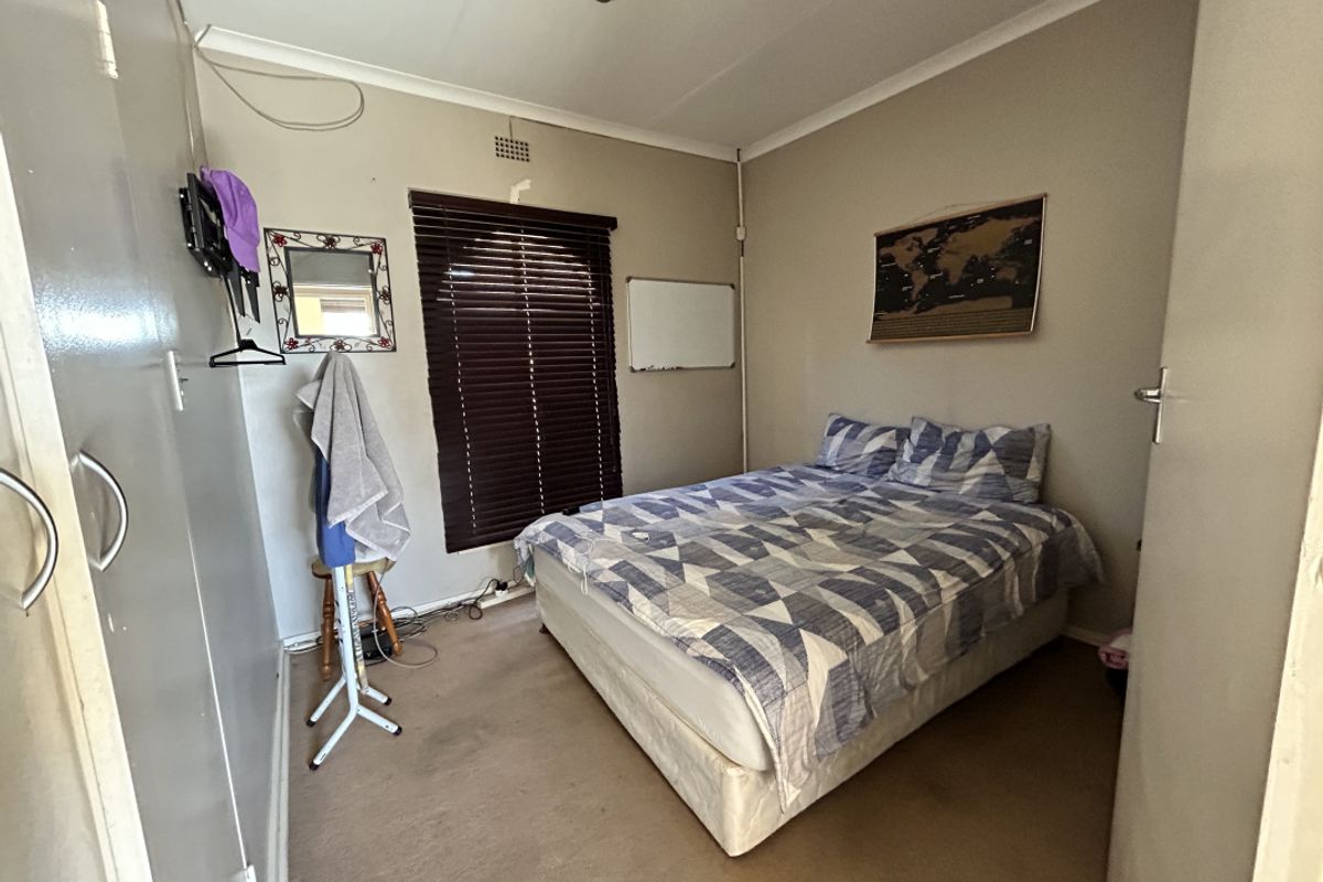 A compact bedroom featuring built-in cupboards, venetian blinds, and carpeted flooring. The space would benefit from cosmetic updates to finishes.