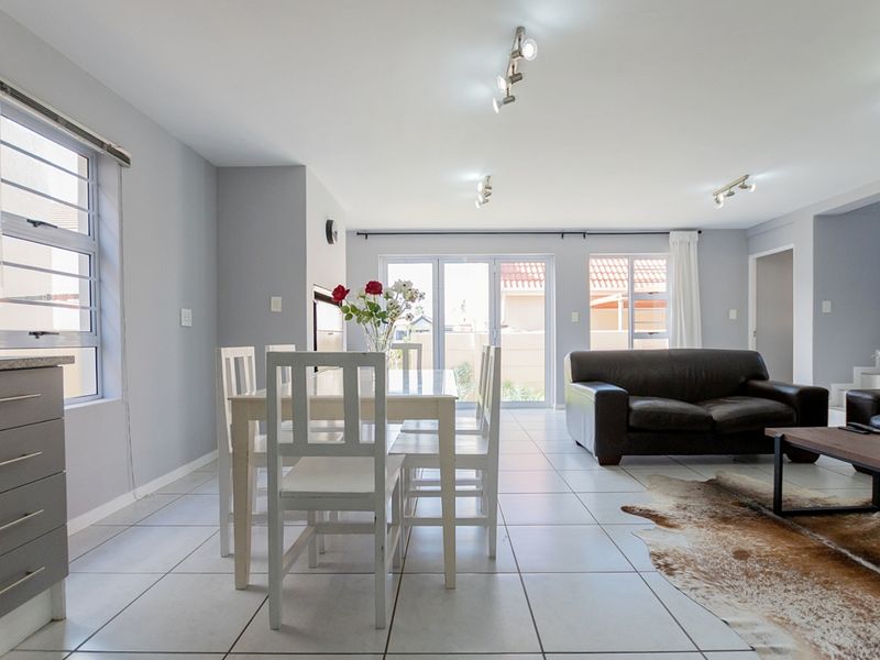 Spacious open-plan living and dining area featuring neutral tiled flooring, modern track lighting, and large aluminium sliding doors leading to the exterior.